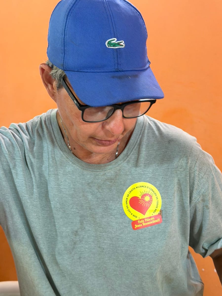 Pessoa de boné azul usa no peito o adesivo de coração amarelo e vermelho da associação.