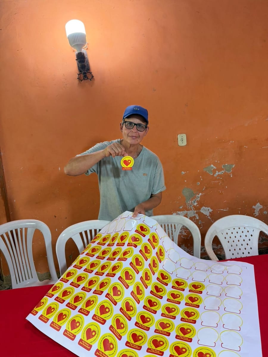 Pessoa de boné segura uma cartela inteira de adesivos de coração amarelo sobre uma mesa.