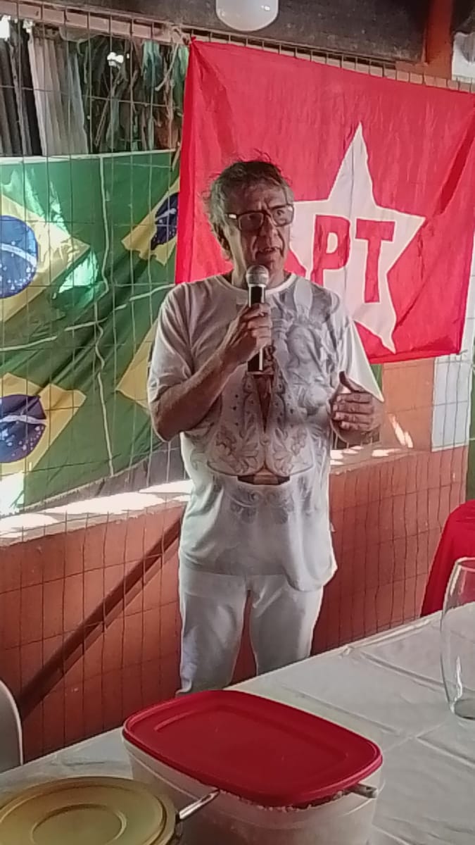 Homem de cabelos grisalhos fala ao microfone diante das bandeiras do partido e do Brasil.