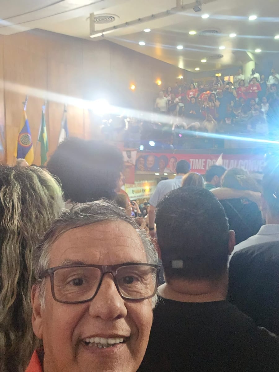 Homem sorri em primeiro plano dentro de um auditório lotado durante um encontro do partido.