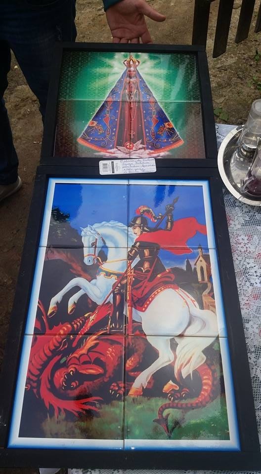 Dois painéis de azulejo com imagens religiosas sendo segurados ao ar livre.