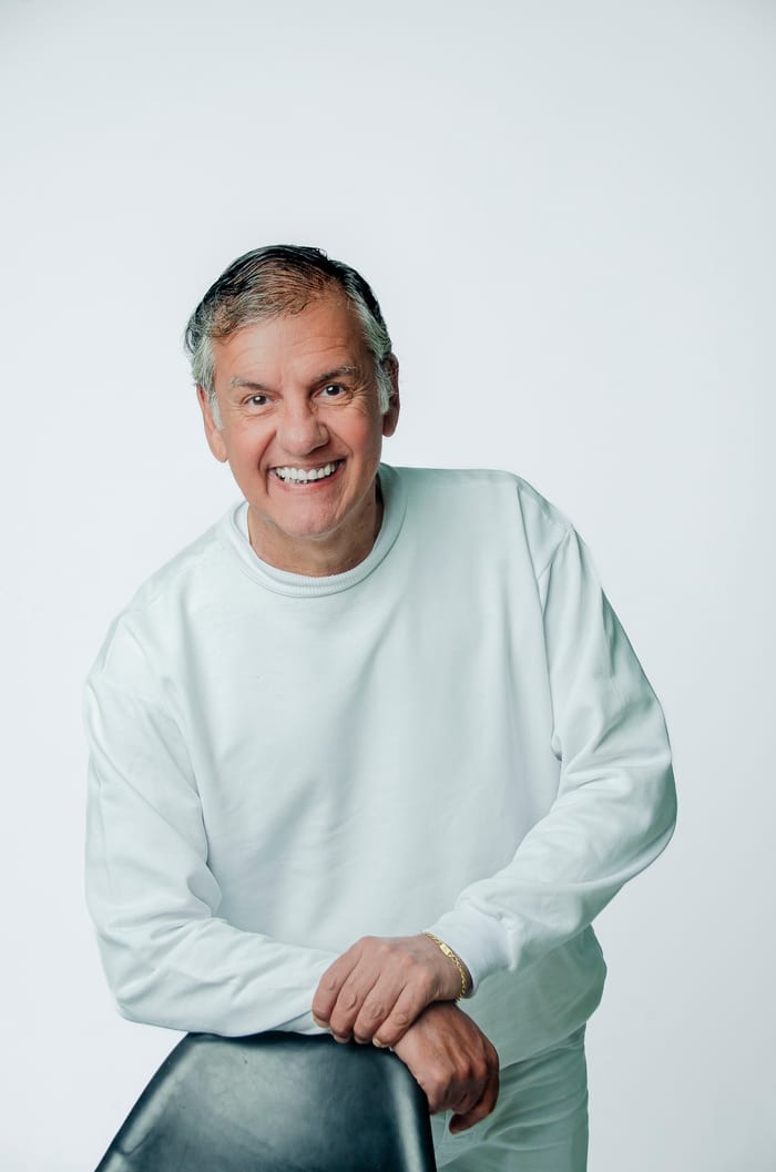 Dr. Marquinho Barreto de pé, apoiado numa cadeira, vestindo roupa branca e sorrindo.