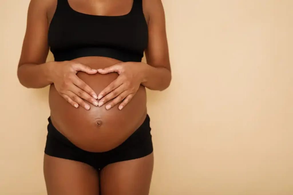 Mulher grávida com as mãos formando um coração sobre a barriga.
