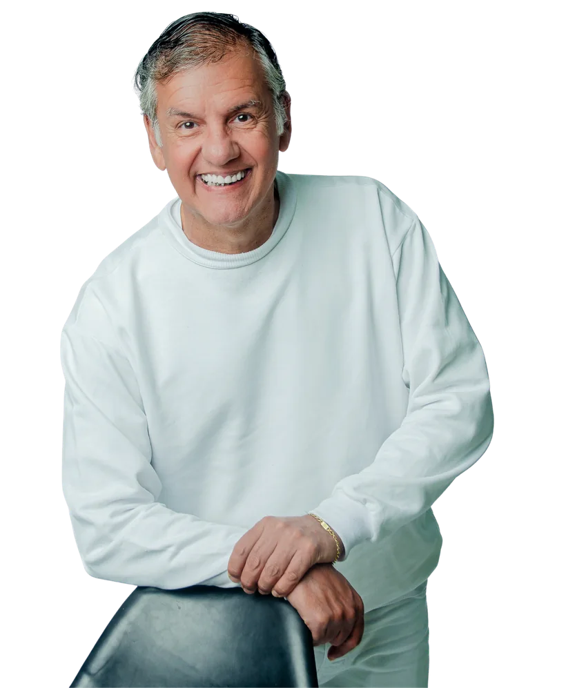 Dr. Marquinho Barreto de pé, apoiado numa cadeira, vestindo roupa branca e sorrindo.
