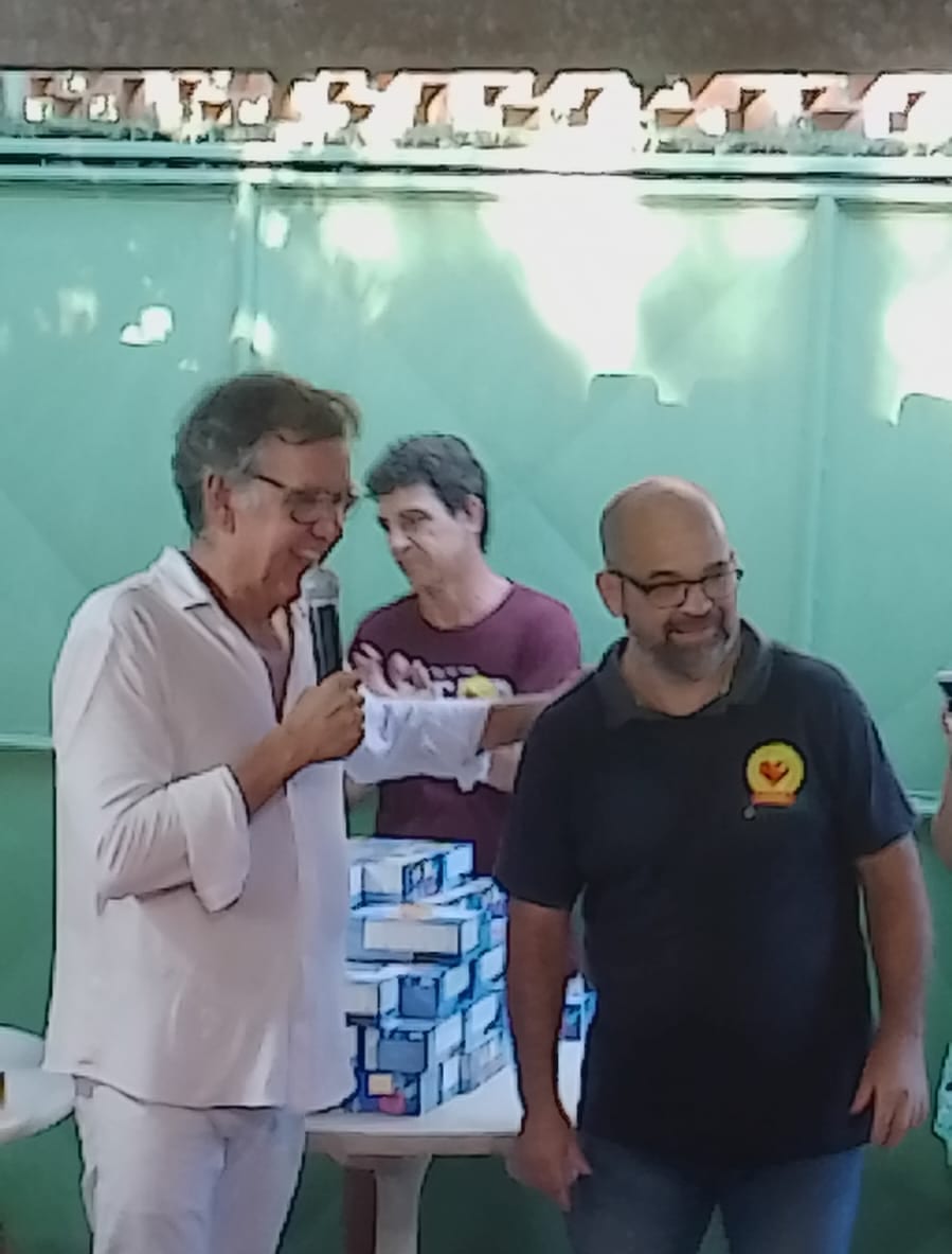 Dr. Marquinho Barreto ao microfone, ao lado de dois apoiadores, junto a caixas empilhadas sobre uma mesa.