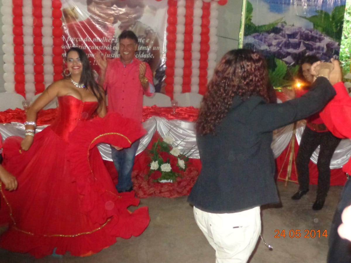 Mulher de vestido vermelho dançando diante de uma faixa com mensagem sobre a força da mulher.